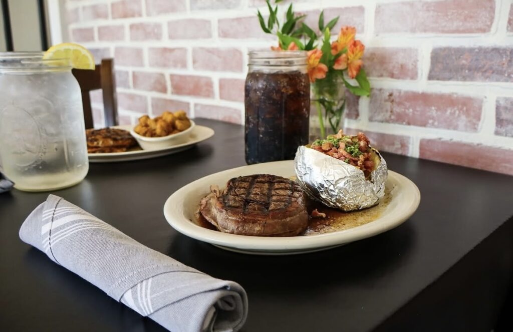Steak and baked potatoes on plates with a brick backdrop and drinks in mason jars in Memphis TN